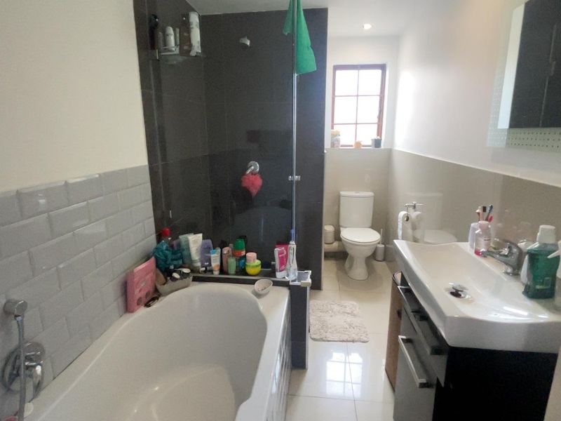A functional bathroom featuring a bathtub, separate shower area with dark tiling, a modern vanity basin, and a toilet.