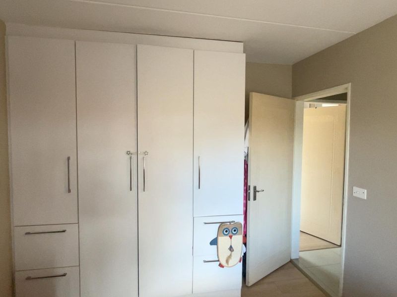A bedroom featuring a large white built-in wardrobe with integrated drawers and a standard internal door leading to an adjacent room.