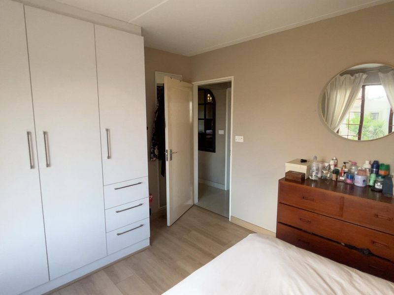 A functional bedroom featuring light-toned laminate flooring and a large, modern white built-in wardrobe with ample storage space.