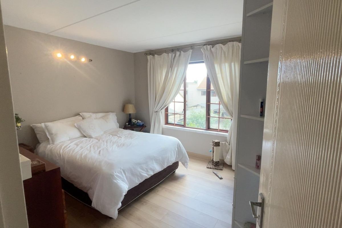 A well-lit bedroom featuring light-toned laminate flooring, built-in shelving, and a window with natural light.