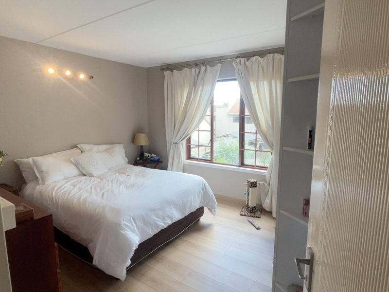 A well-lit bedroom featuring light-toned laminate flooring, built-in shelving, and a window with natural light.