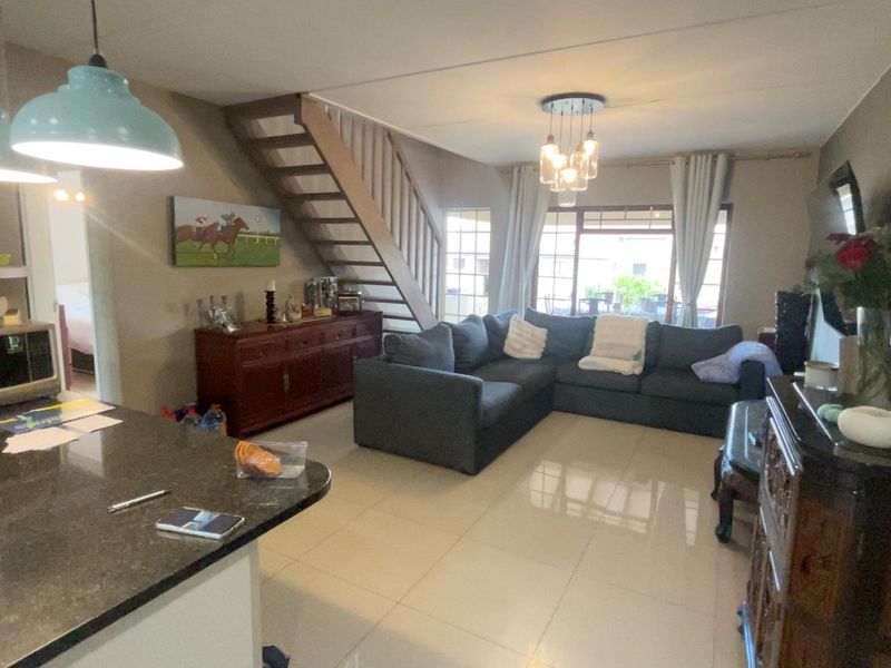 Spacious open-plan living area featuring tiled floors, a modern staircase, and a kitchen with granite countertops, flowing seamlessly to the outdoor patio area.