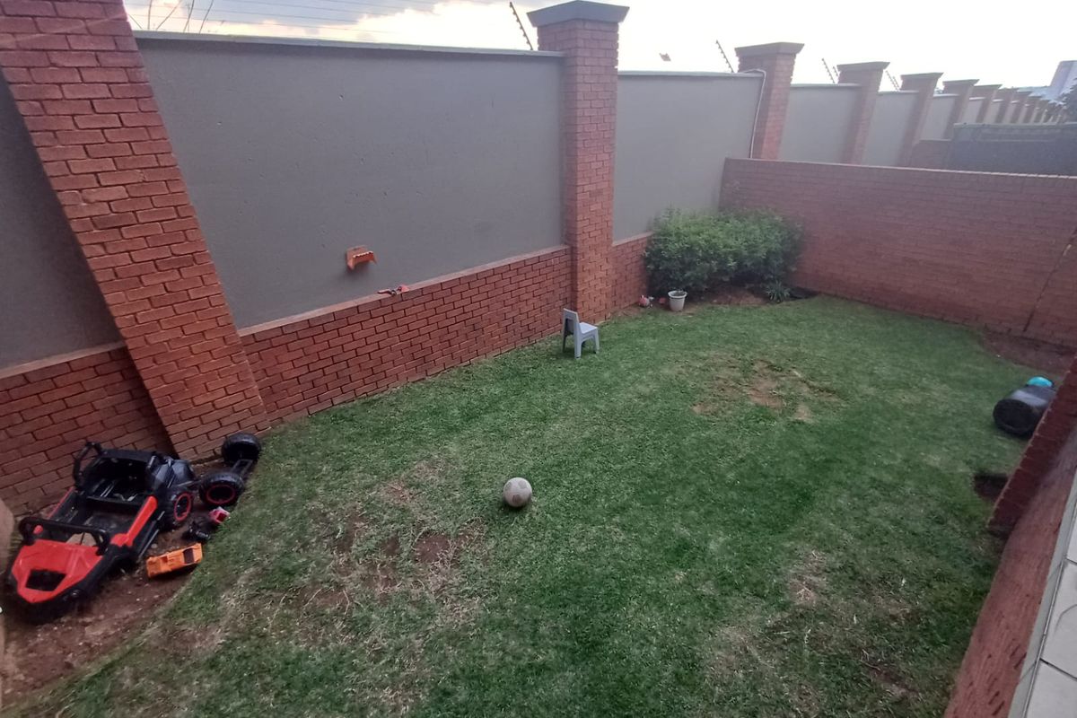 A private rear garden area featuring a lawn enclosed by high brick boundary walls with integrated electric fencing.