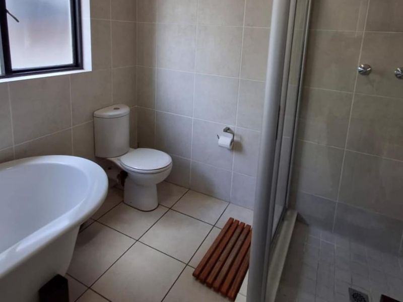 A functional bathroom featuring a freestanding bathtub, a separate shower enclosure, and neutral wall and floor tiling.