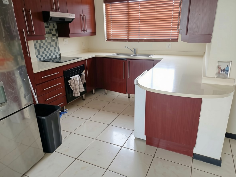 A functional kitchen featuring dark wood cabinetry, stone countertops, integrated appliances, and tiled flooring with a window providing natural light.