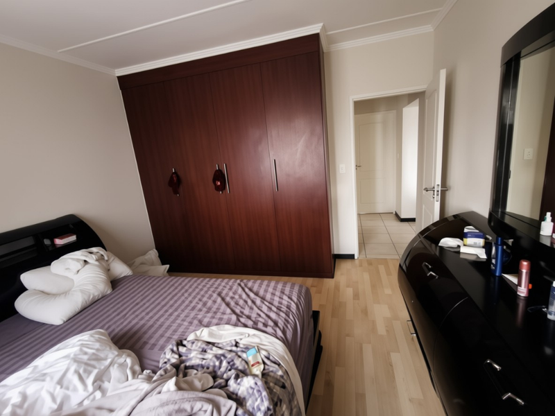 A bedroom featuring a large dark wood built-in wardrobe, light laminate flooring, and coved ceiling details, with an adjacent hallway visible.