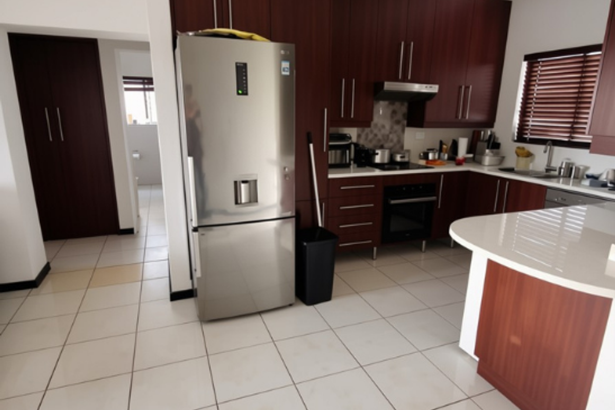 A functional kitchen featuring dark wood cabinetry, stone countertops, built-in oven, extractor fan, and tiled flooring with a breakfast bar area.