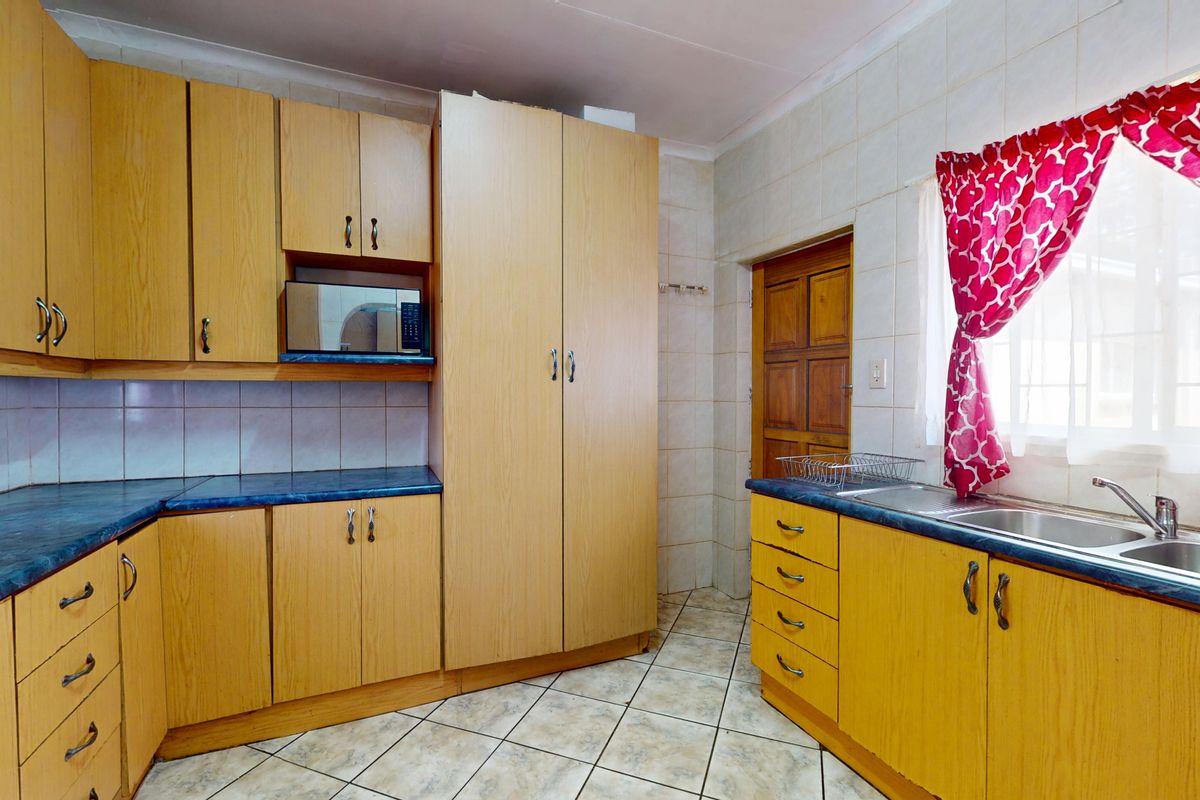 A functional kitchen featuring light wood-tone cabinetry, blue laminate countertops, a double stainless steel sink, and tiled flooring with a neutral splashback.