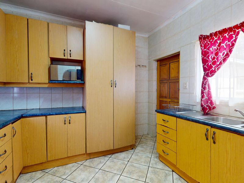A functional kitchen featuring light wood-tone cabinetry, blue laminate countertops, a double stainless steel sink, and tiled flooring with a neutral splashback.