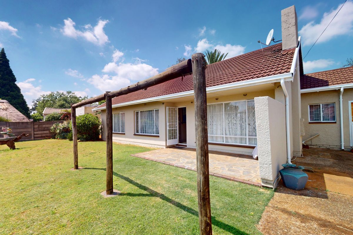 Rear view of the house featuring a tiled roof, chimney, and a stone-paved patio area overlooking the garden.