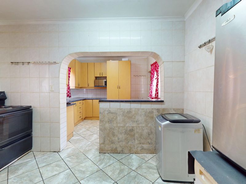 A functional kitchen featuring tiled walls and flooring, built-in cabinetry, and a breakfast counter with an arched opening connecting to the adjacent space.