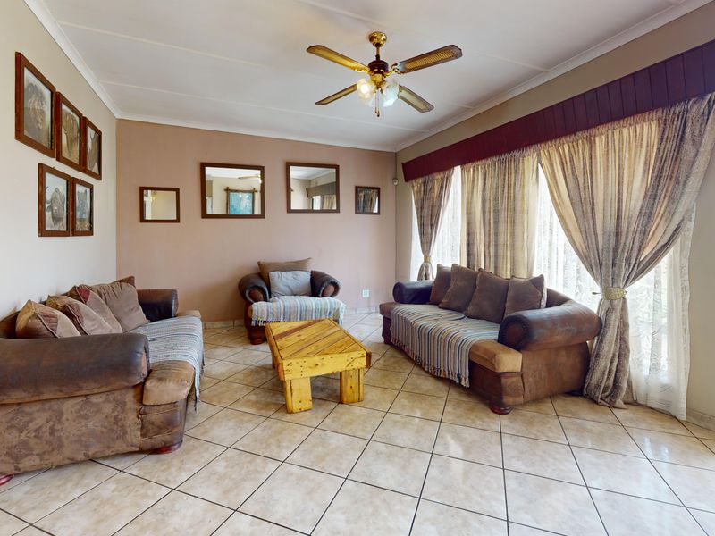 A spacious living room featuring tiled flooring, a ceiling fan, and large windows with decorative pelmets, offering a comfortable and functional living space.