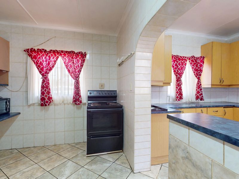 A functional kitchen featuring tiled walls and flooring, laminate cabinetry, and a central archway connecting to an adjacent prep area.