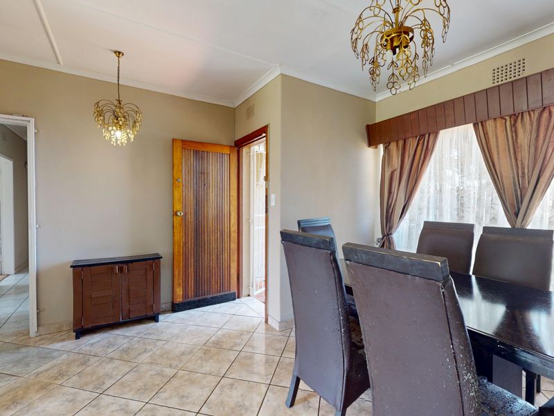 A dining room featuring tiled flooring, decorative chandeliers, and access to adjacent rooms, offering a functional space with potential for modern updates.