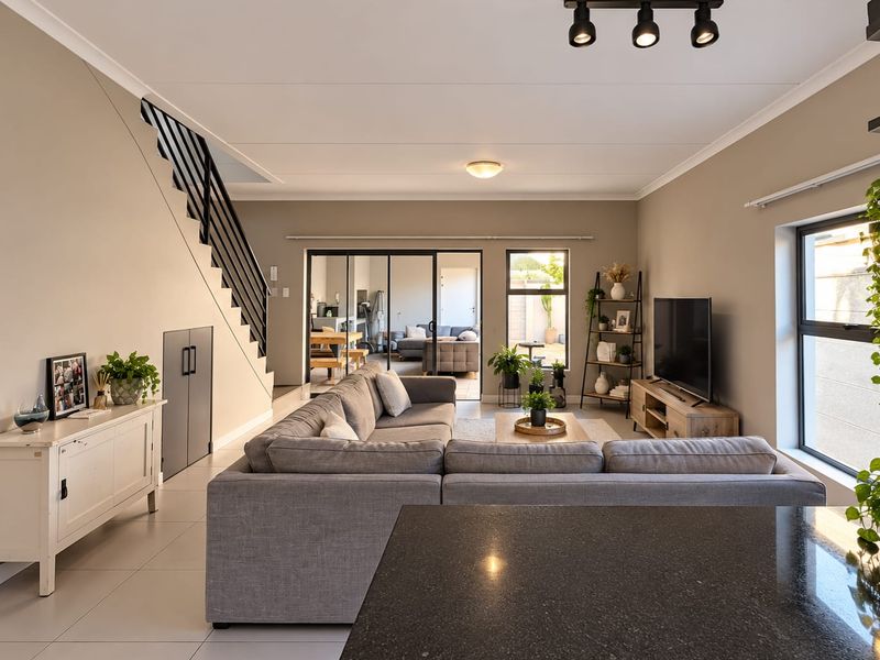 Spacious open-plan living area featuring modern tiled floors, a sleek staircase with metal balustrades, and large sliding glass doors leading to the patio.