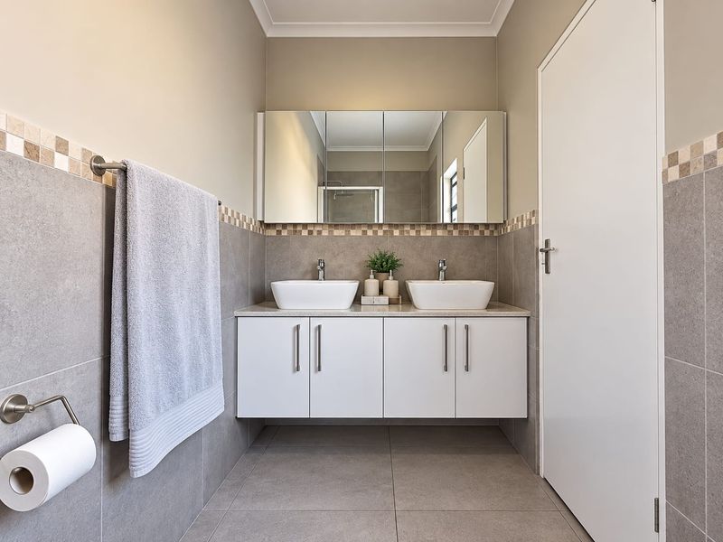 Modern bathroom featuring a double vanity with vessel sinks, a large mirrored cabinet, and neutral grey wall and floor tiling.