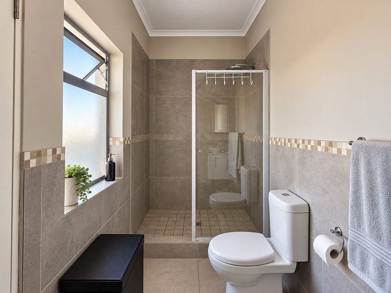 A well-maintained bathroom featuring a walk-in shower with a glass enclosure, neutral wall tiling, and a modern toilet.