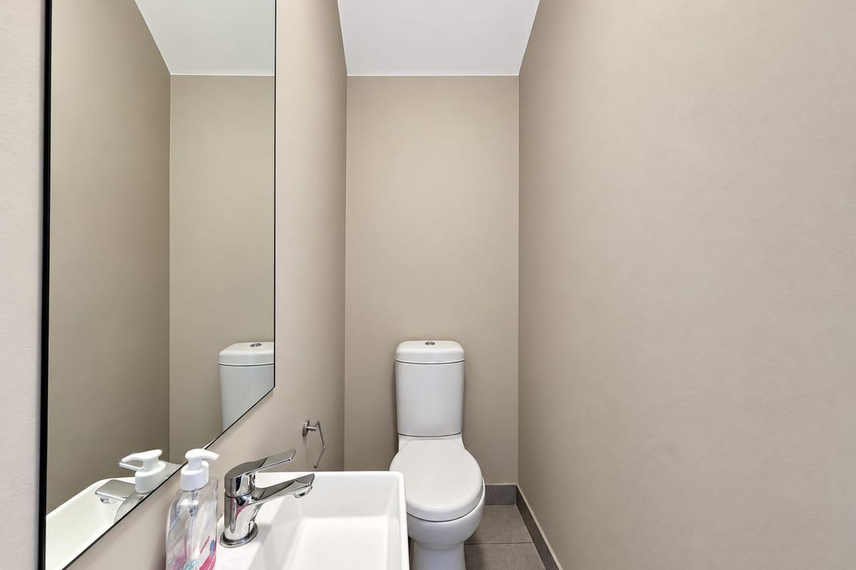 A compact powder room featuring a modern ceramic basin with chrome mixer tap, wall-mounted mirror, and a standard toilet.