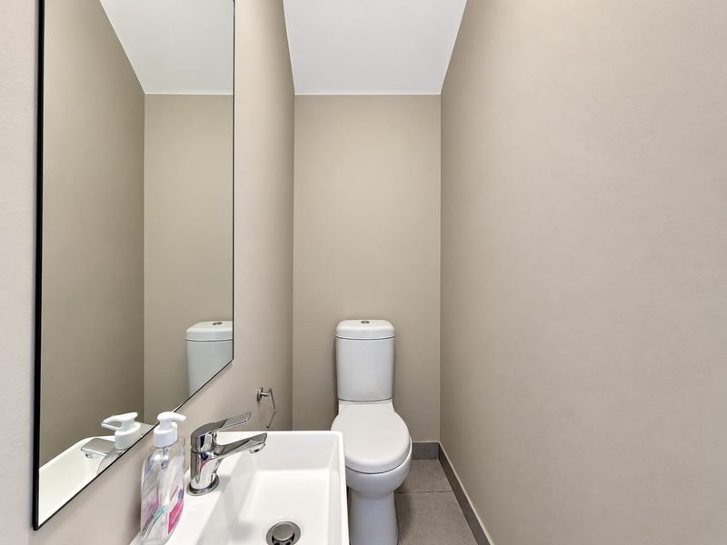 A compact powder room featuring a modern ceramic basin with chrome mixer tap, wall-mounted mirror, and a standard toilet.