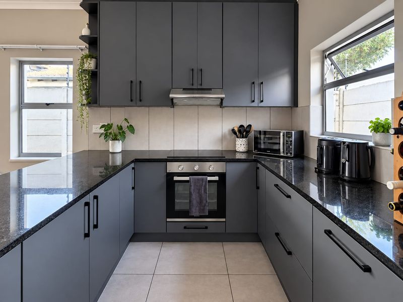 Modern U-shaped kitchen featuring dark grey cabinetry, sleek granite countertops, built-in oven, hob, and extractor fan with neutral tiled flooring.