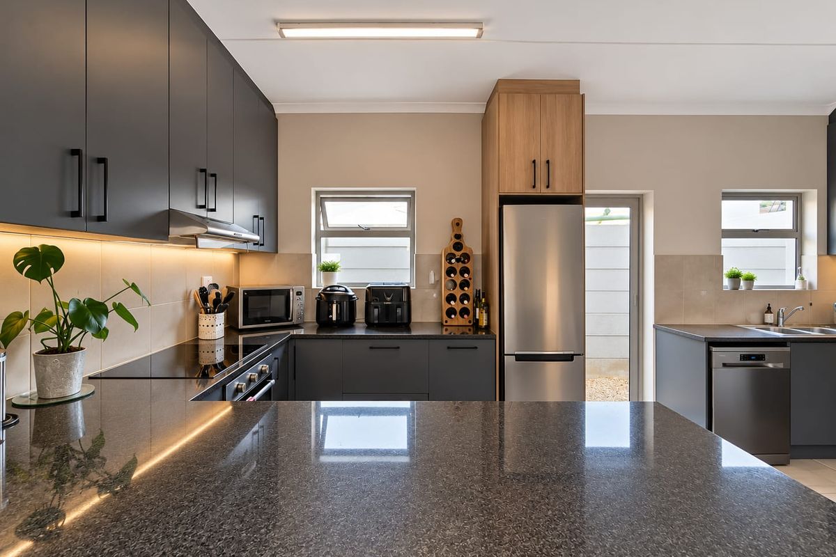 Modern kitchen featuring sleek dark cabinetry, granite countertops, integrated appliances, and efficient under-cabinet lighting, offering a clean and functional culinary space.