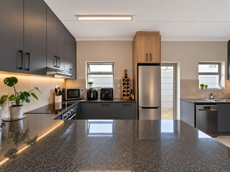 Modern kitchen featuring sleek dark cabinetry, granite countertops, integrated appliances, and efficient under-cabinet lighting, offering a clean and functional culinary space.