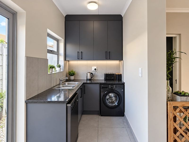 Modern scullery featuring dark grey cabinetry, granite countertops, stainless steel sink, and integrated laundry and dishwasher appliances with sleek tiled flooring.