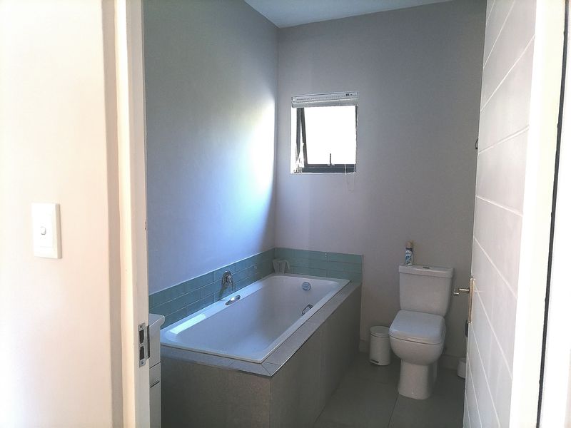 A functional bathroom featuring a built-in bathtub with tiled splashback, a standard toilet, and a window for natural light.