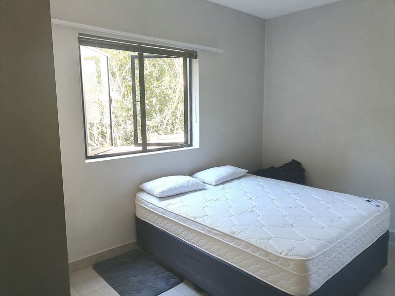 A simple bedroom featuring neutral walls, tiled flooring, and a window providing natural light.