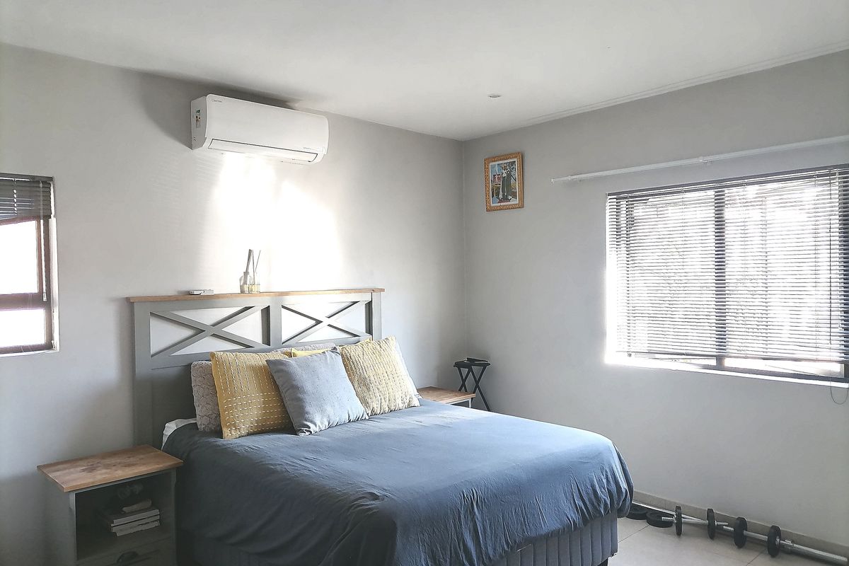A well-lit bedroom featuring tiled flooring, venetian blinds, and a wall-mounted split-system air conditioning unit.