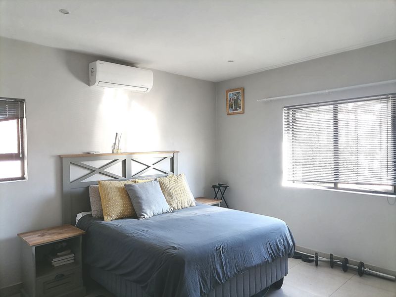 A well-lit bedroom featuring tiled flooring, venetian blinds, and a wall-mounted split-system air conditioning unit.