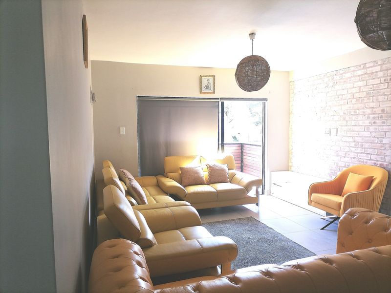 A living room featuring tiled flooring, an exposed brick feature wall, and a sliding glass door leading to an outdoor area.