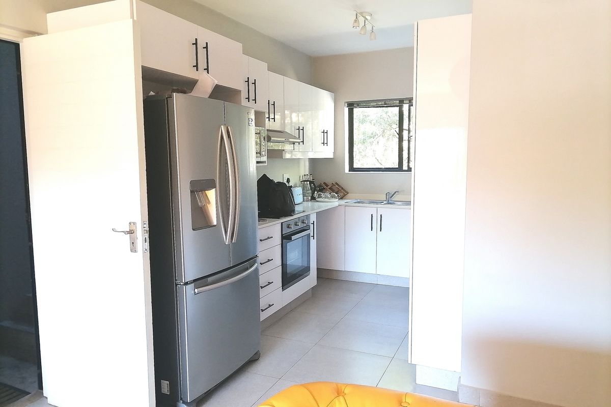 A functional kitchen featuring white cabinetry, built-in oven and hob, extractor fan, and tiled flooring, offering a clean and modern aesthetic.