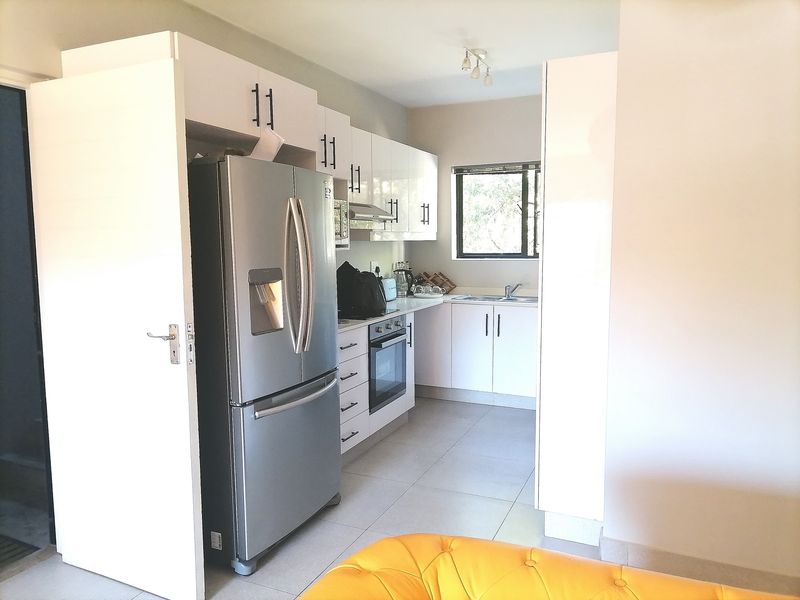 A functional kitchen featuring white cabinetry, built-in oven and hob, extractor fan, and tiled flooring, offering a clean and modern aesthetic.