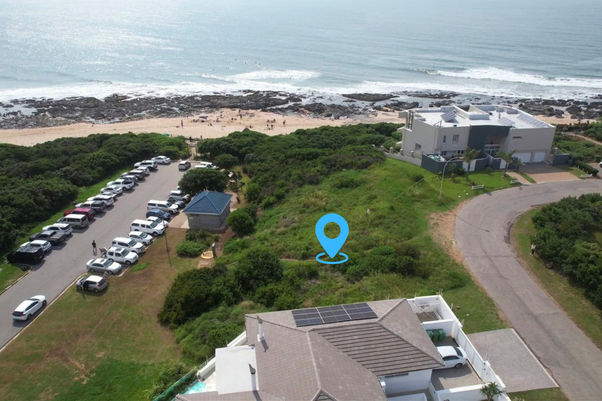 Aerial view of a vacant residential plot situated in a prime coastal location, adjacent to beach access and public parking facilities.