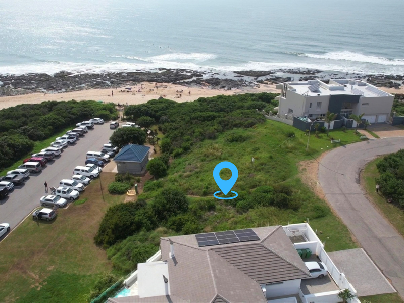 Aerial view of a vacant residential plot situated in a prime coastal location, adjacent to beach access and public parking facilities.