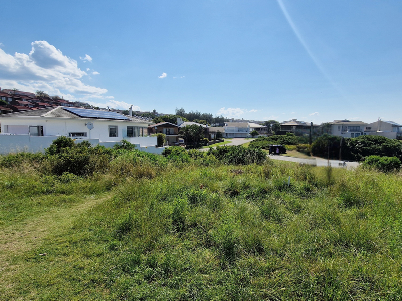 A view of a vacant residential plot featuring natural grassland and coastal vegetation, situated in a developed neighborhood.
