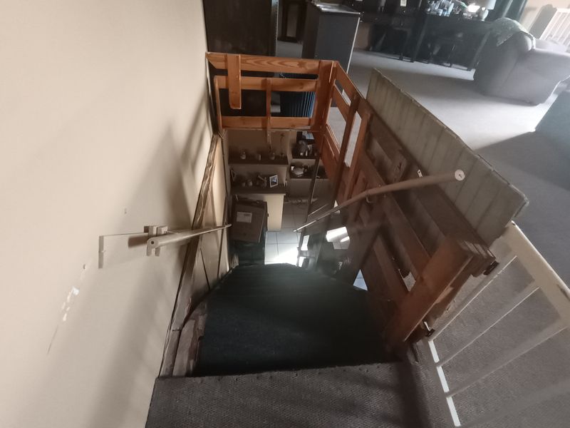 A steep staircase featuring a wooden balustrade and carpeted steps, showing signs of wear and requiring maintenance or renovation.