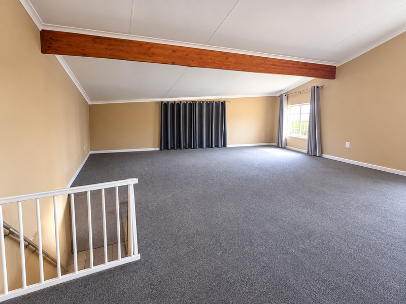 A spacious, empty living area featuring a vaulted ceiling with an exposed timber beam, neutral walls, and carpeted flooring.