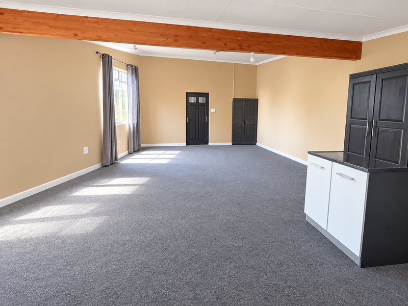 Spacious living area featuring an exposed timber ceiling beam, neutral walls, carpeted flooring, and built-in storage cabinetry.