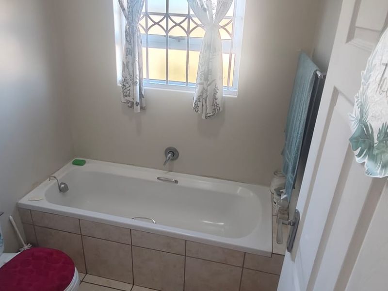 A functional bathroom featuring a built-in bathtub with tiled surround, a toilet, and a window with security bars.
