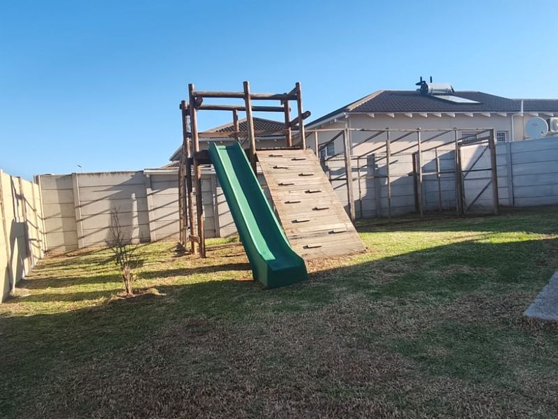 A rear garden area featuring a precast concrete boundary wall, a lawn, and a wooden play structure.