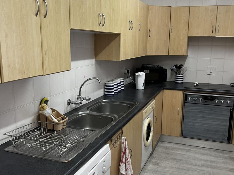 Functional kitchen featuring light wood-tone cabinetry, dark countertops, a double stainless steel sink, and integrated oven with tiled wall finishes.