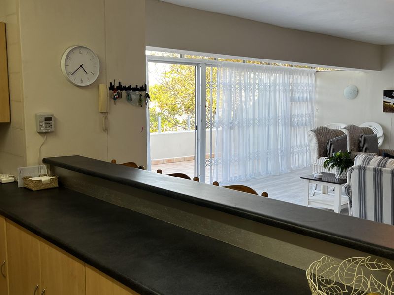 Open plan kitchen with breakfast bar overlooking a bright living area and balcony with sliding glass doors.