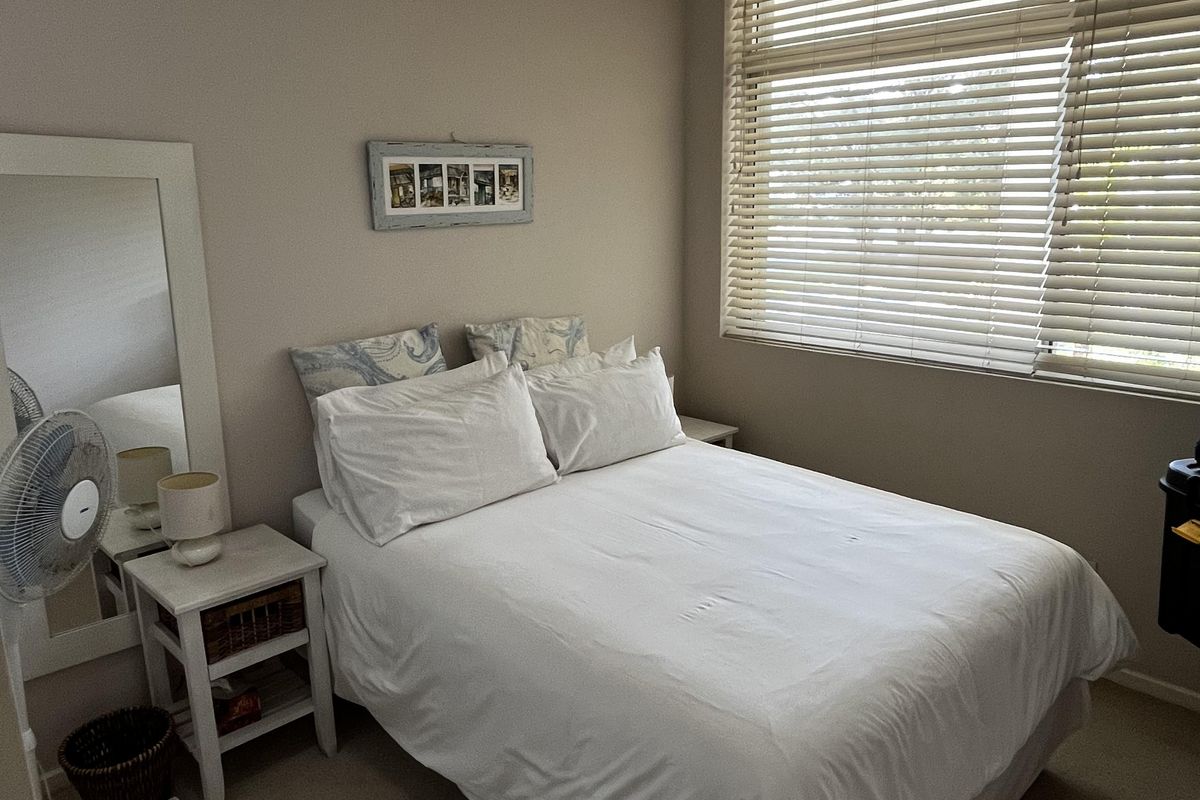 A functional bedroom featuring neutral wall tones, carpeted flooring, and large windows fitted with venetian blinds for adjustable natural light.