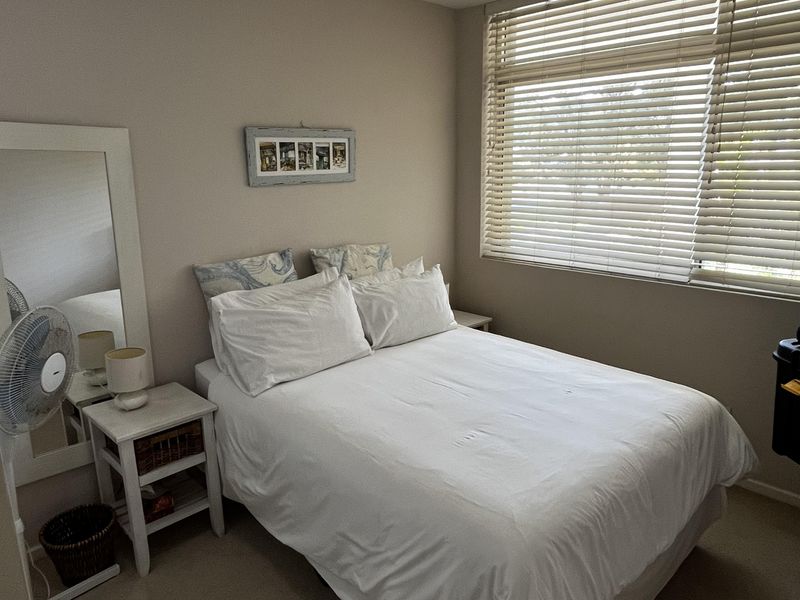 A functional bedroom featuring neutral wall tones, carpeted flooring, and large windows fitted with venetian blinds for adjustable natural light.