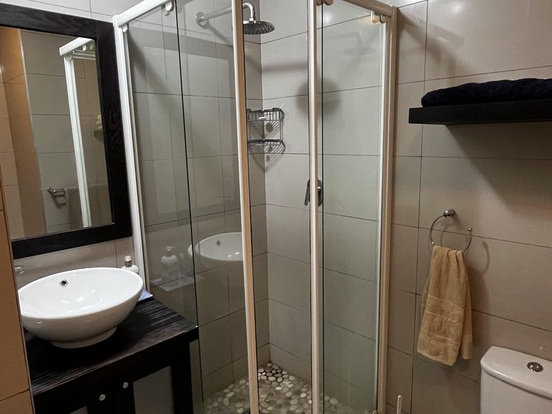 A compact, modern bathroom featuring a glass shower enclosure with a pebble floor, a dark wood vanity with a vessel sink, and a standard toilet.