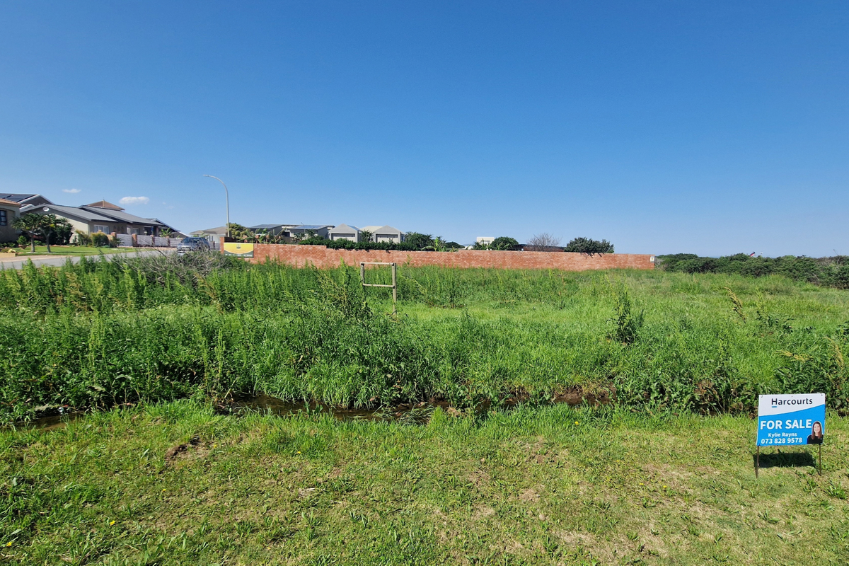 A vacant residential plot featuring a grassed surface and a brick boundary wall, situated in a developed neighborhood.