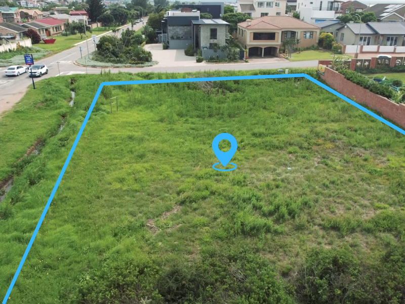 Aerial view of a vacant residential plot featuring grassed land and a boundary wall, situated in a developed neighborhood.