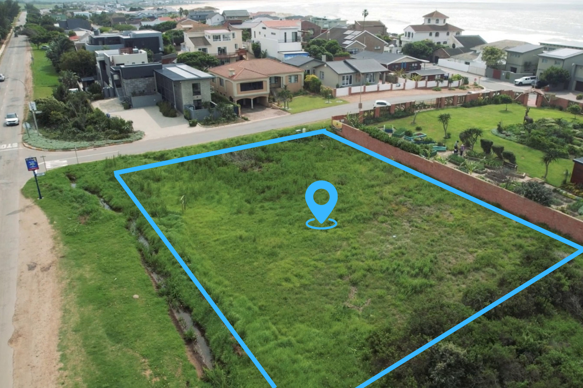 An aerial view of a vacant residential plot situated in a coastal neighborhood, featuring grass cover and proximity to existing residential properties.